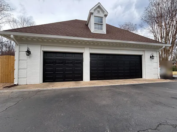 Two black raised-panel garage doors on a white brick garage