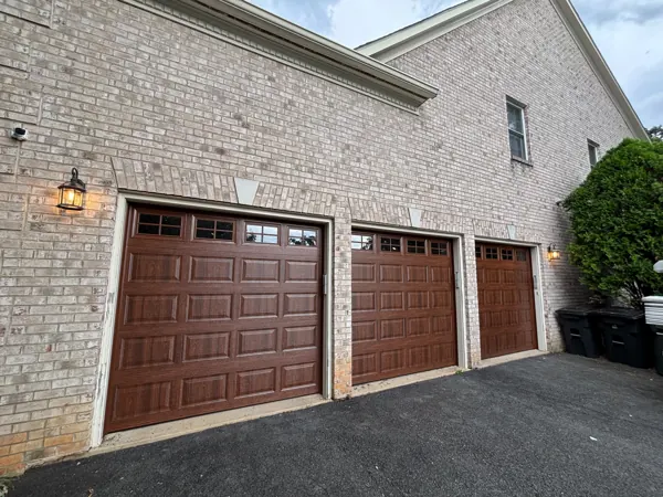 Three new woodgrain raised-panel garage doors with windows on a brick home