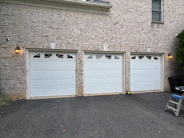 Three white garage doors on a brick home before the upgrade